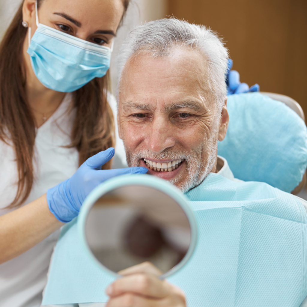 Elderly patient looking in the mirror at their smile after dental treatment